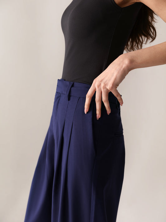 A close-up of a woman's navy wide-leg pants with double pleats, showing the fabric and design details.