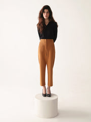 Woman wearing a black top and beltless high waisted pants on a white background