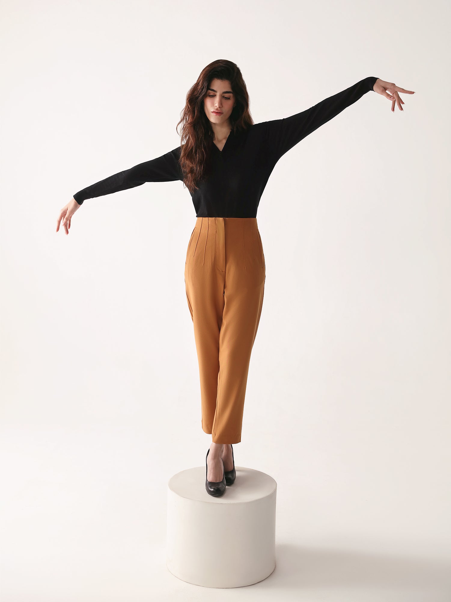 A model wearing high-waisted, beltless brown high waisted pants with seam details on the front and back.