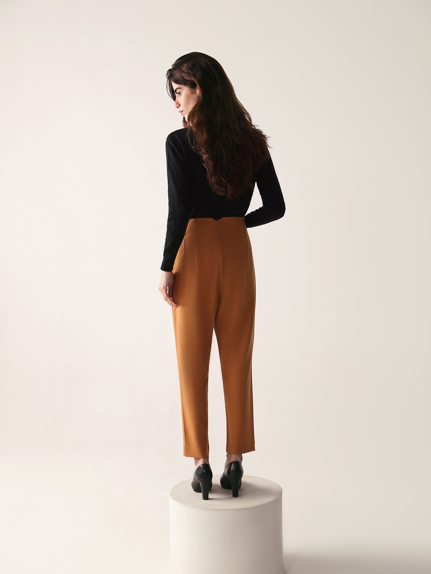A model wearing high-waisted, beltless brown high waisted pants with seam details on the front and back.