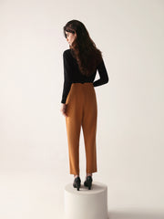A model wearing high-waisted, beltless brown high waisted pants with seam details on the front and back.