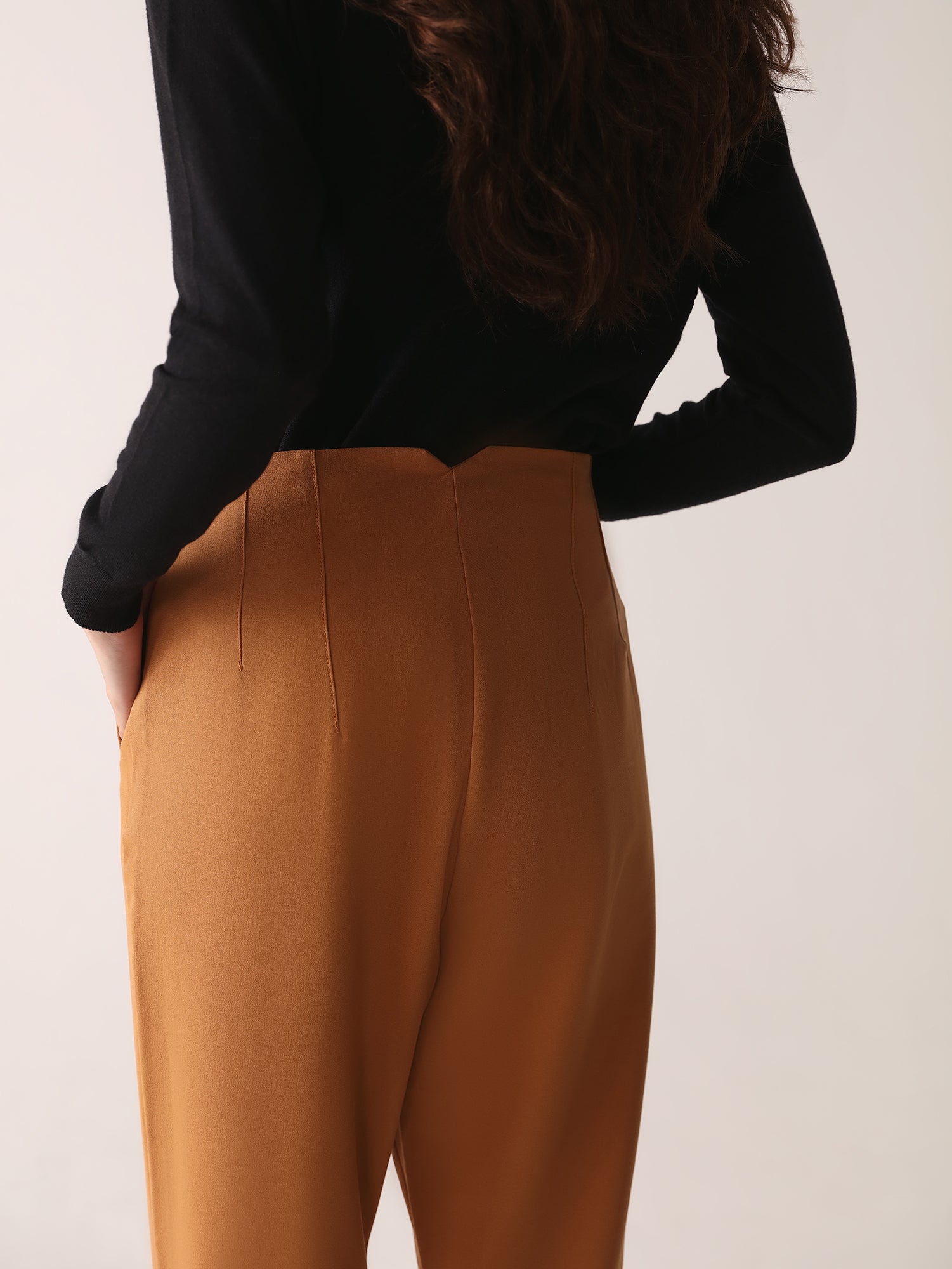A model wearing high-waisted, beltless brown high waisted pants with seam details on the front and back.