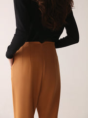A model wearing high-waisted, beltless brown high waisted pants with seam details on the front and back.