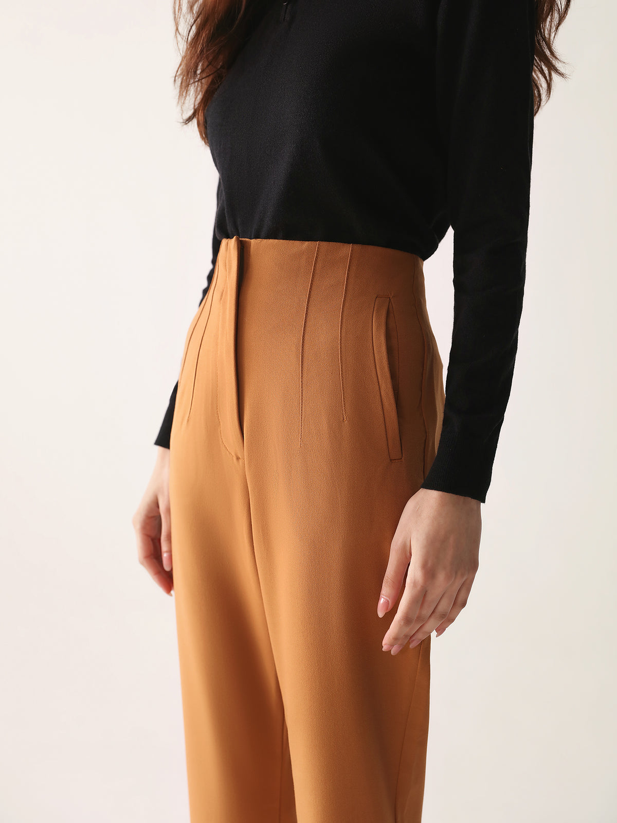 A model wearing high-waisted, beltless brown high waisted pants with seam details on the front and back.