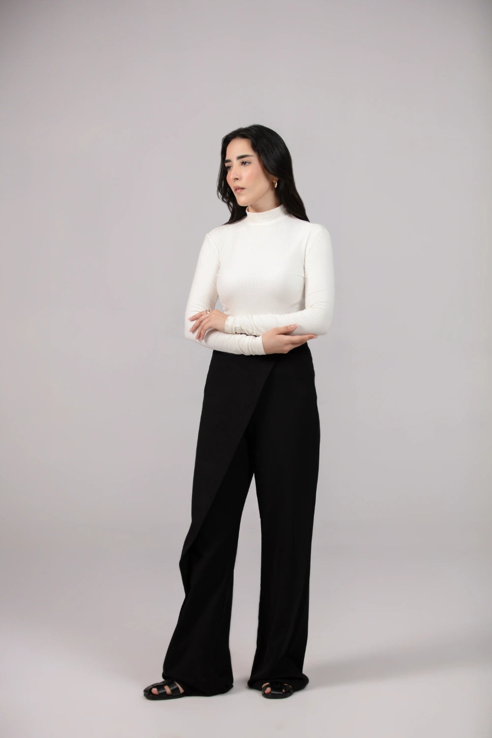 Woman wearing a white turtleneck and black pants on a gray background