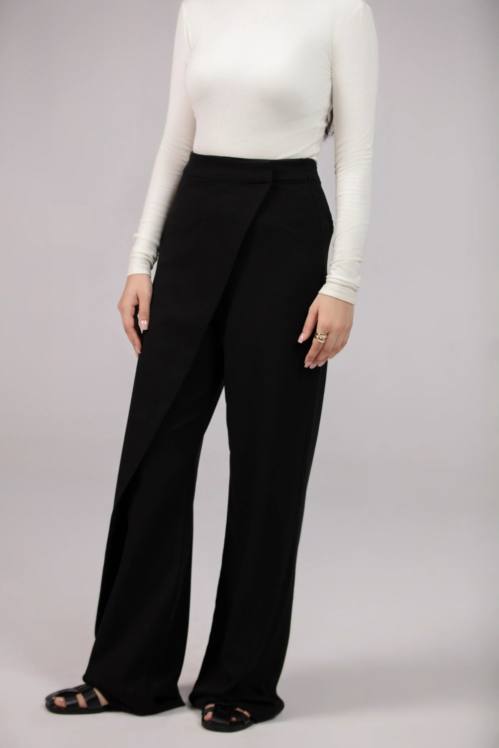 Person wearing a white long-sleeve top and black wide-leg pants on a plain background