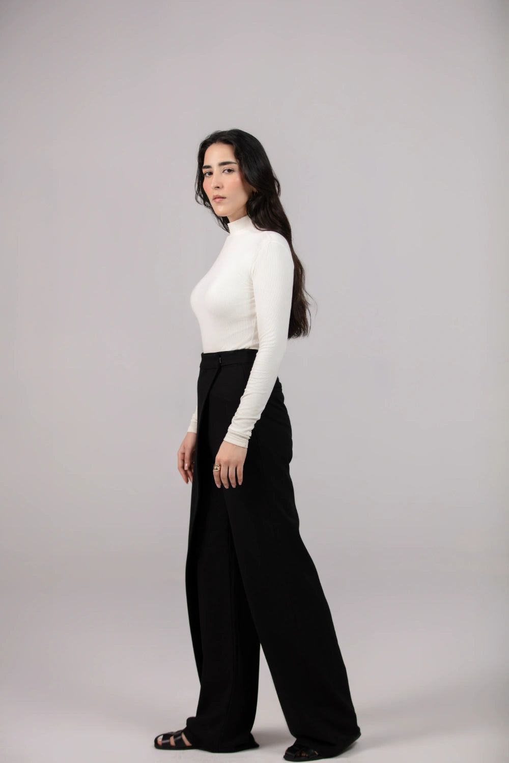 Woman wearing a white top and black wide-leg pants on a gray background