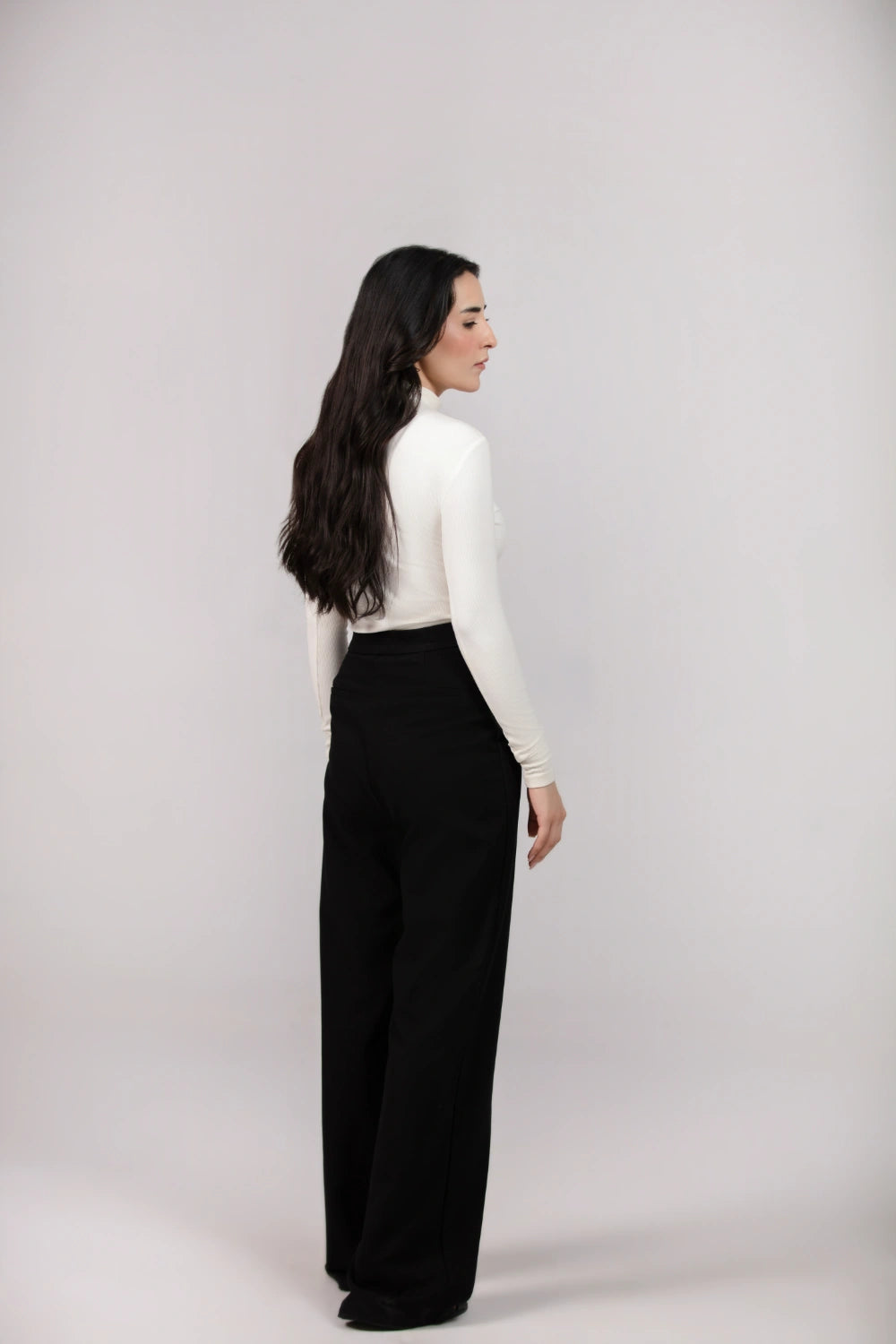Woman wearing a white long-sleeve top and black pants on a light gray background