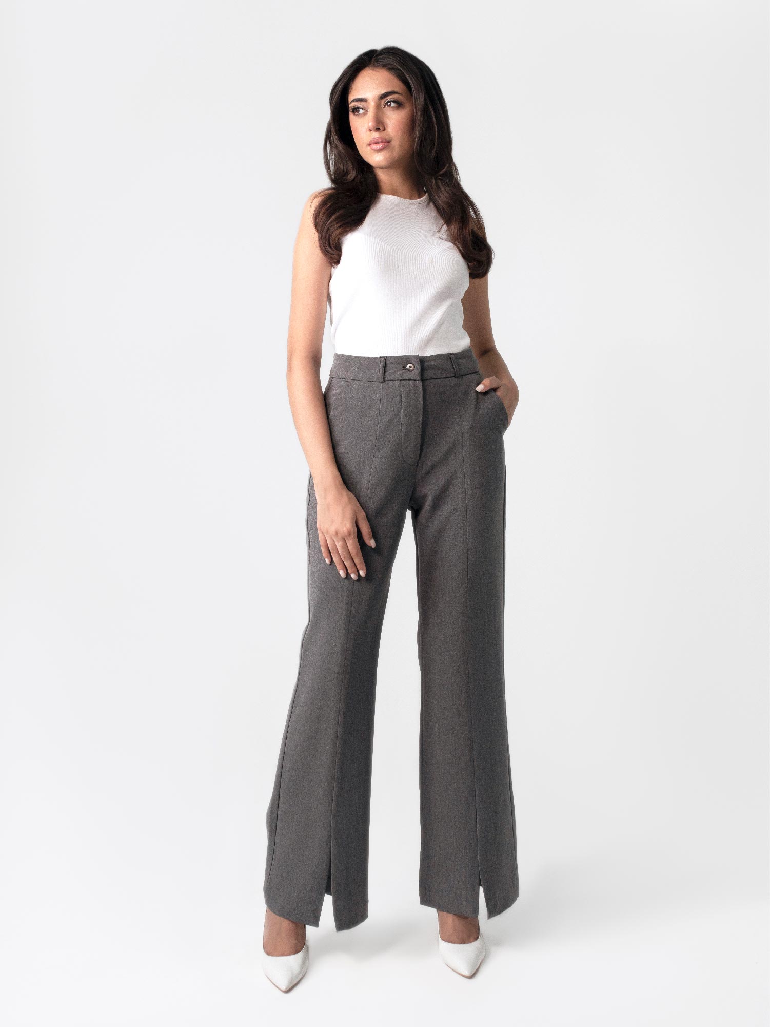A woman in a white top and dark grey flared pants with front slits, fitted waist belt, and cross pockets.