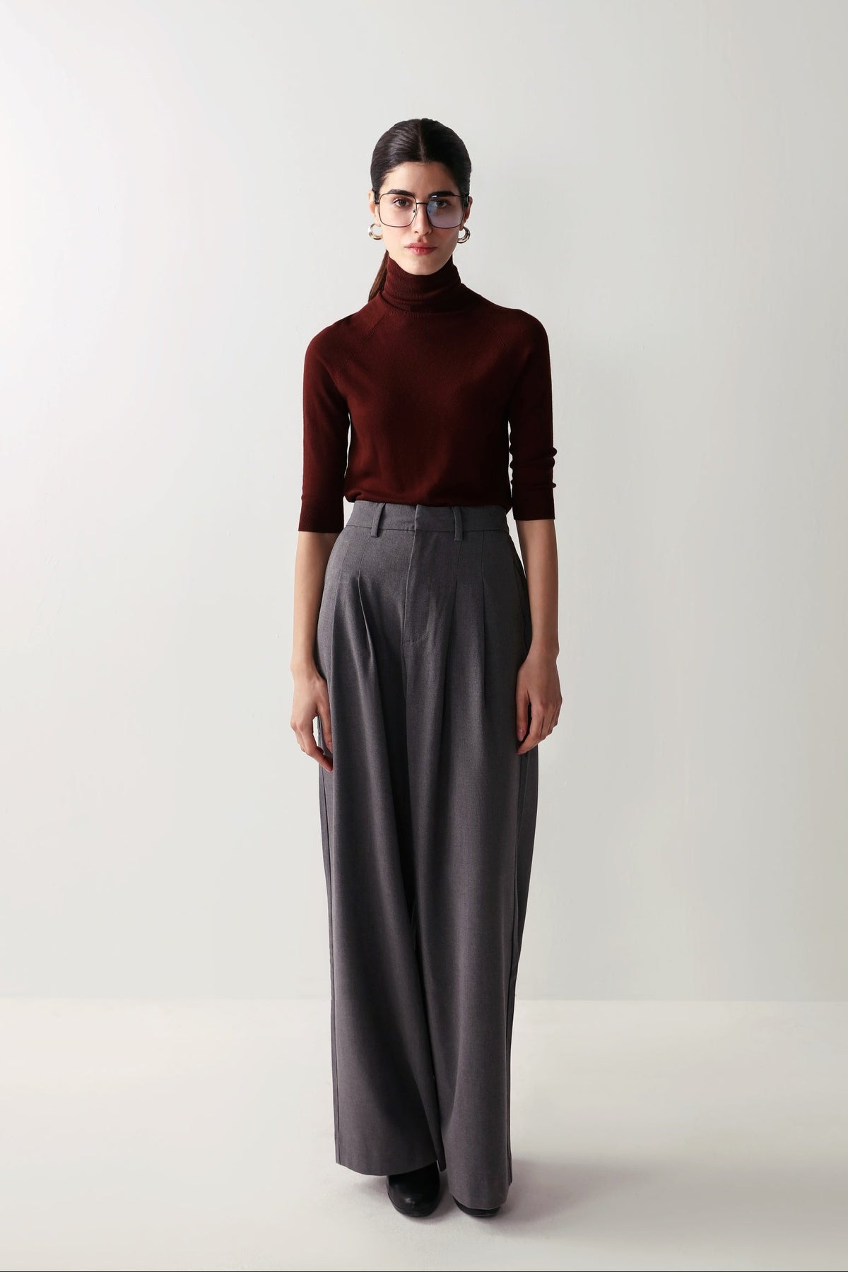 A woman in a maroon top and low-rise grey wide leg pants with pleats and pockets, showcasing a smart, flattering fit.
