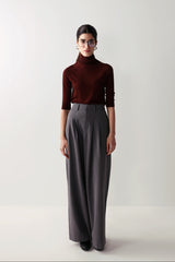 A woman in a maroon top and low-rise grey wide leg pants with pleats and pockets, showcasing a smart, flattering fit.