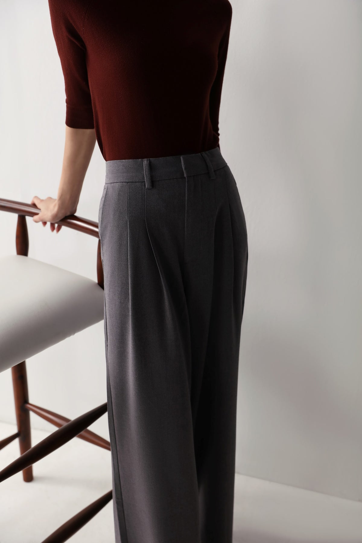 A woman in a maroon top and low-rise grey wide leg pants with pleats and pockets, showcasing a smart, flattering fit.
