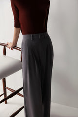 A woman in a maroon top and low-rise grey wide leg pants with pleats and pockets, showcasing a smart, flattering fit.