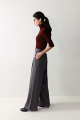 A woman in a maroon top and low-rise grey wide leg pants with pleats and pockets, showcasing a smart, flattering fit.