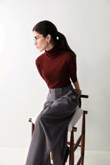 A woman in a maroon top and low-rise grey wide leg pants with pleats and pockets, showcasing a smart, flattering fit.