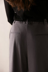 Low-rise black wide leg pants with a fitted belt, pleats, and multiple pockets, designed for a formal and smart look.