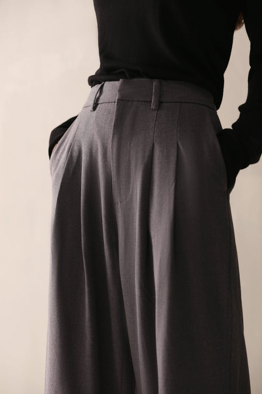 A woman in a black top and low-rise grey wide leg pants with pleats and pockets, showcasing a smart, flattering fit.