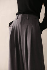 A woman in a black top and low-rise grey wide leg pants with pleats and pockets, showcasing a smart, flattering fit.