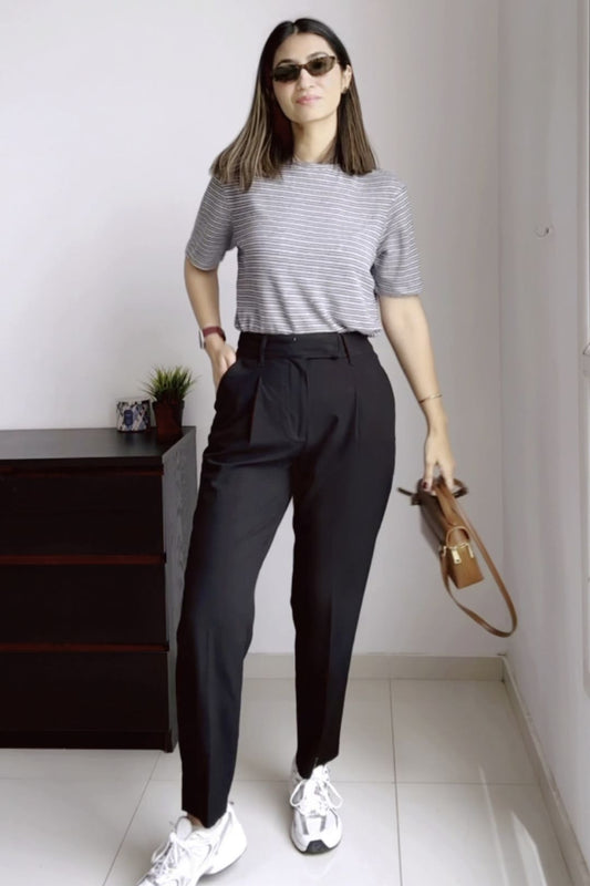 Woman wearing a gray striped shirt, black pants, and white sneakers in a room.