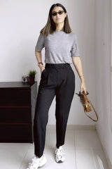 Woman wearing a gray striped shirt, black pants, and white sneakers in a room.