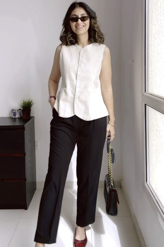 Woman wearing a white sleeveless top and black pants standing in a room with a window.
