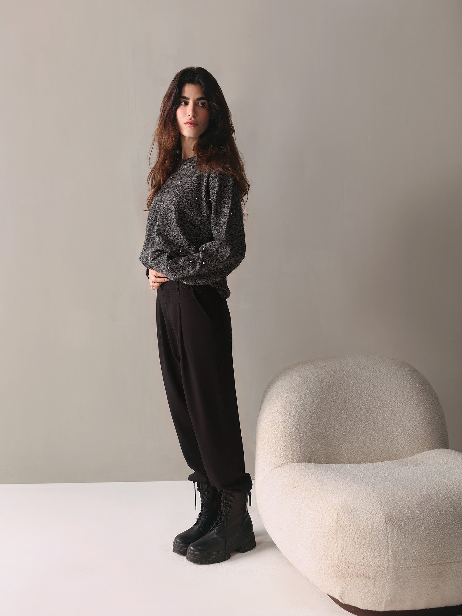 Woman wearing a gray striped shirt, black pants, and white sneakers in a room.