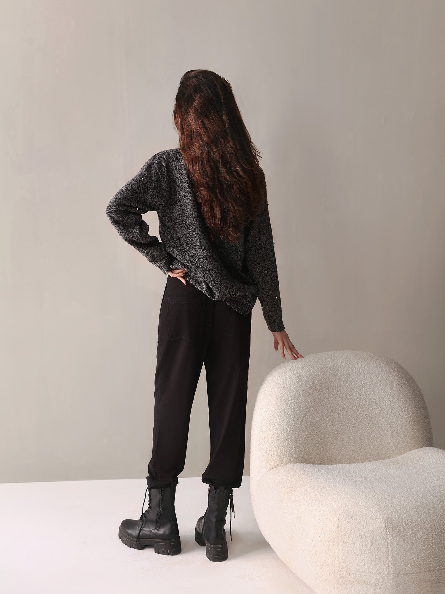 Woman wearing a gray striped shirt, black pants, and black sneakers in a room.