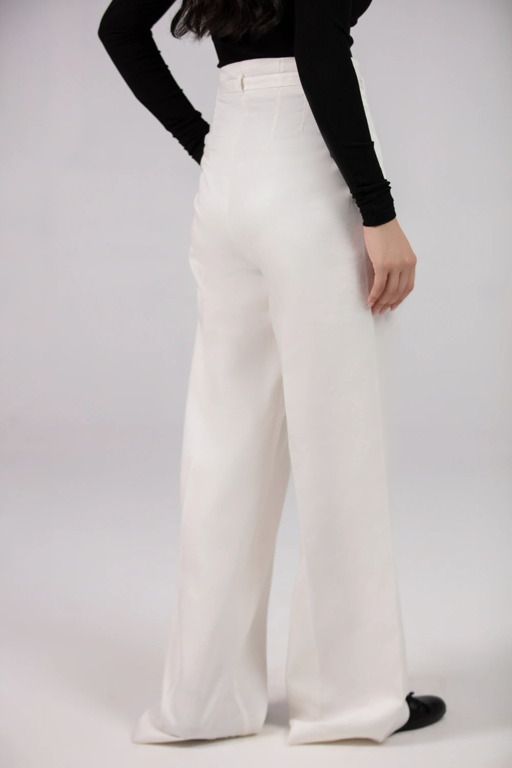 Person wearing white wide-leg pants and a black top on a plain background