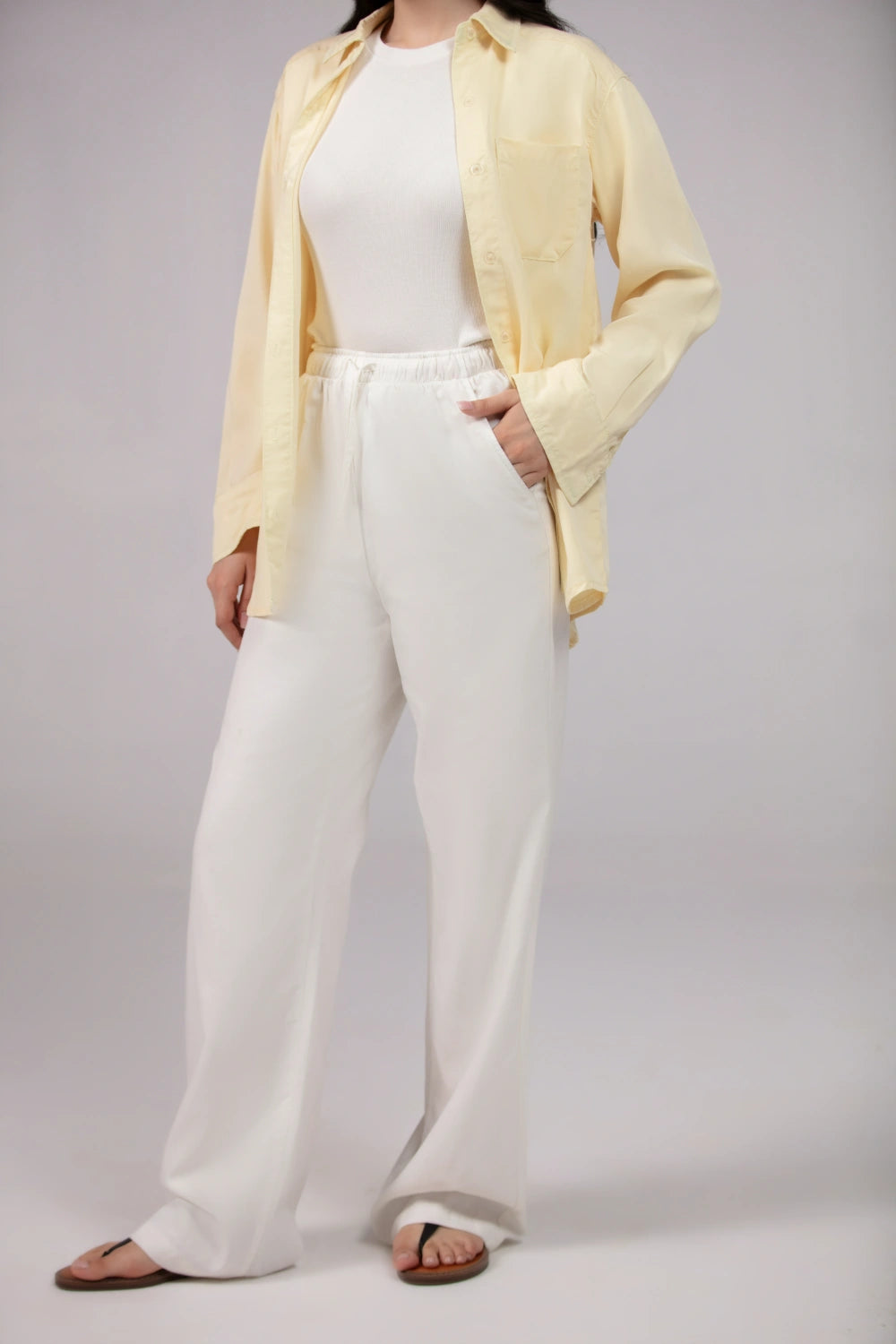 Person wearing a light yellow cardigan, white top, and wide-leg pants on a plain background