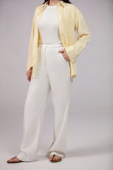 Person wearing a light yellow cardigan, white top, and wide-leg pants on a plain background