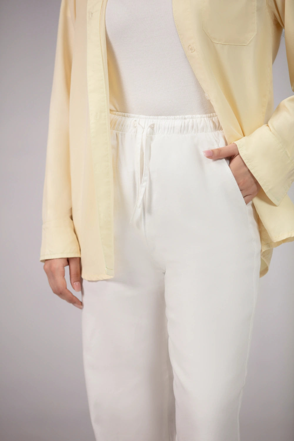 Person wearing a light yellow cardigan over a white top and pants on a plain background
