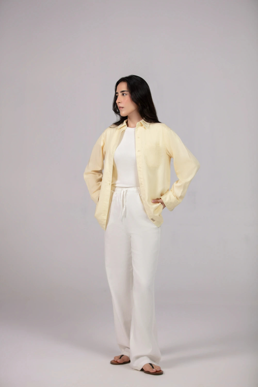 Woman wearing a light yellow jacket over a white outfit on a plain background