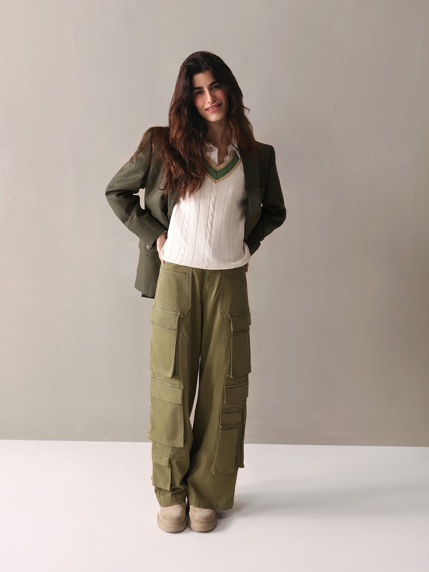 A woman dressed in olive green cargo pants and a white sweater stands confidently, showcasing a casual yet stylish look.