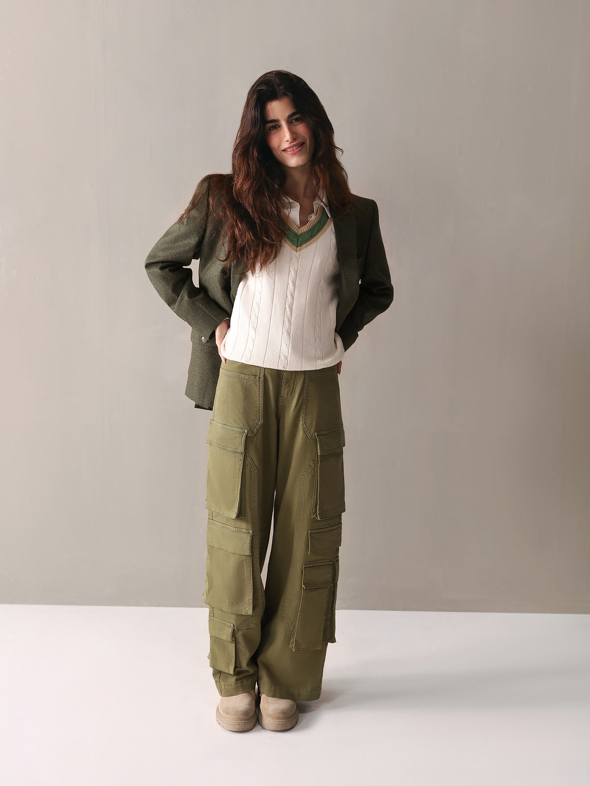 A woman dressed in olive green cargo pants and a white sweater stands confidently, showcasing a casual yet stylish look.