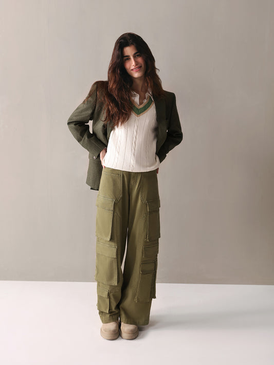 A woman dressed in olive green cargo pants and a white sweater stands confidently, showcasing a casual yet stylish look.