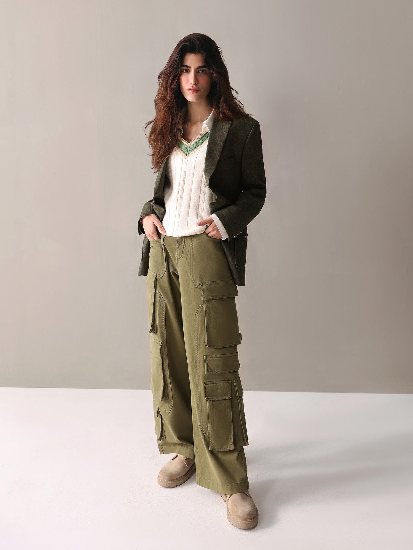 Woman wearing a green blazer and cargo pants against a plain background