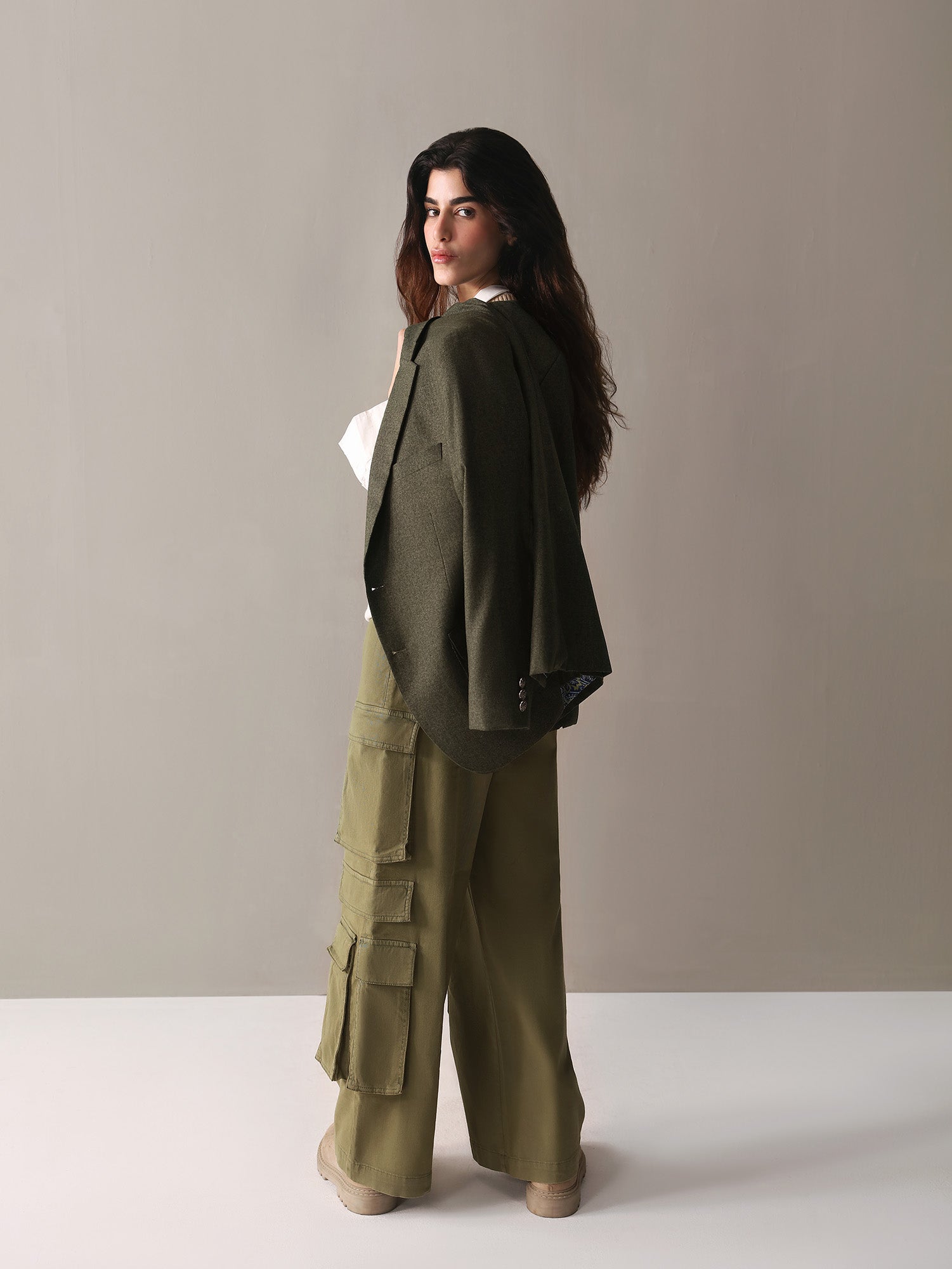  A woman dressed in olive green cargo pants and a white sweater stands confidently, showcasing a casual yet stylish look.
