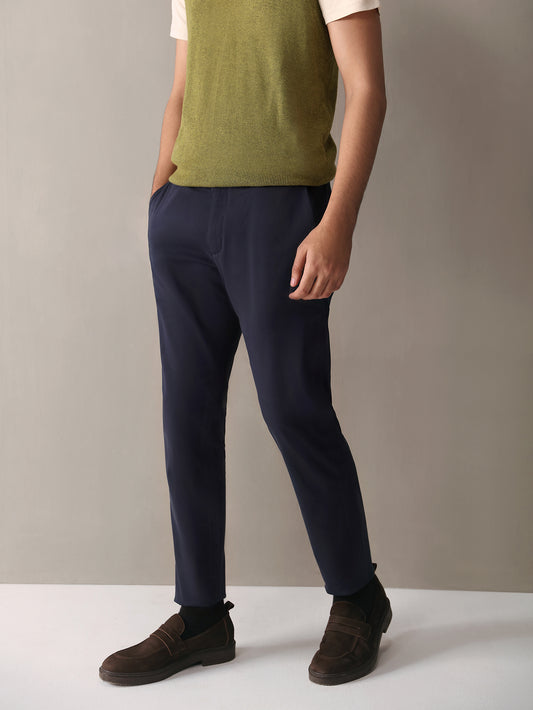A man standing wearing navy slim fit chinos and a green turtleneck vest.