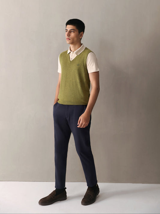 Man wearing a green vest over a white shirt with navy pants against a plain background
