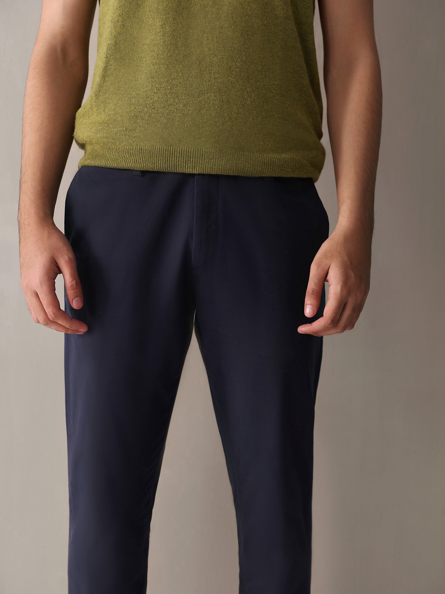 A man standing wearing navy slim fit chinos and a green turtleneck vest.