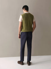 Person wearing a green vest over a white shirt with dark pants against a plain background