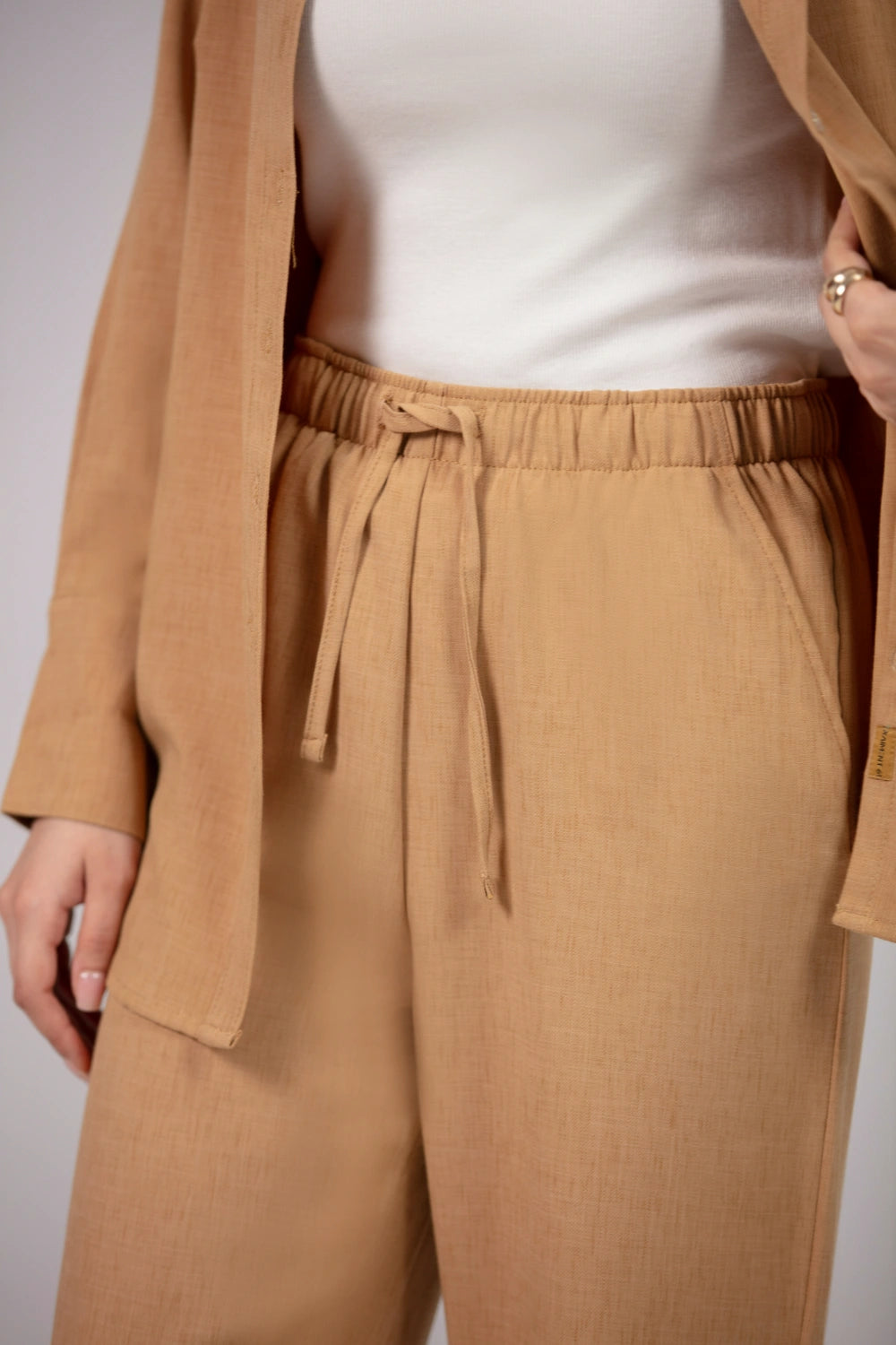 Person wearing a beige coat, white top, and tan pants against a neutral background
