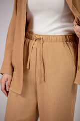 Person wearing a beige coat, white top, and tan pants against a neutral background