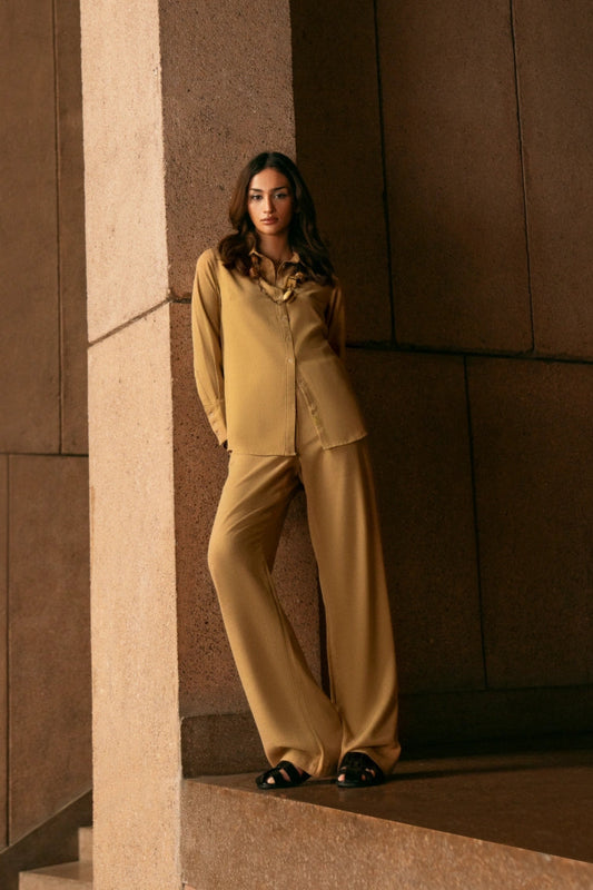 Woman in a beige suit standing against a brown wall.