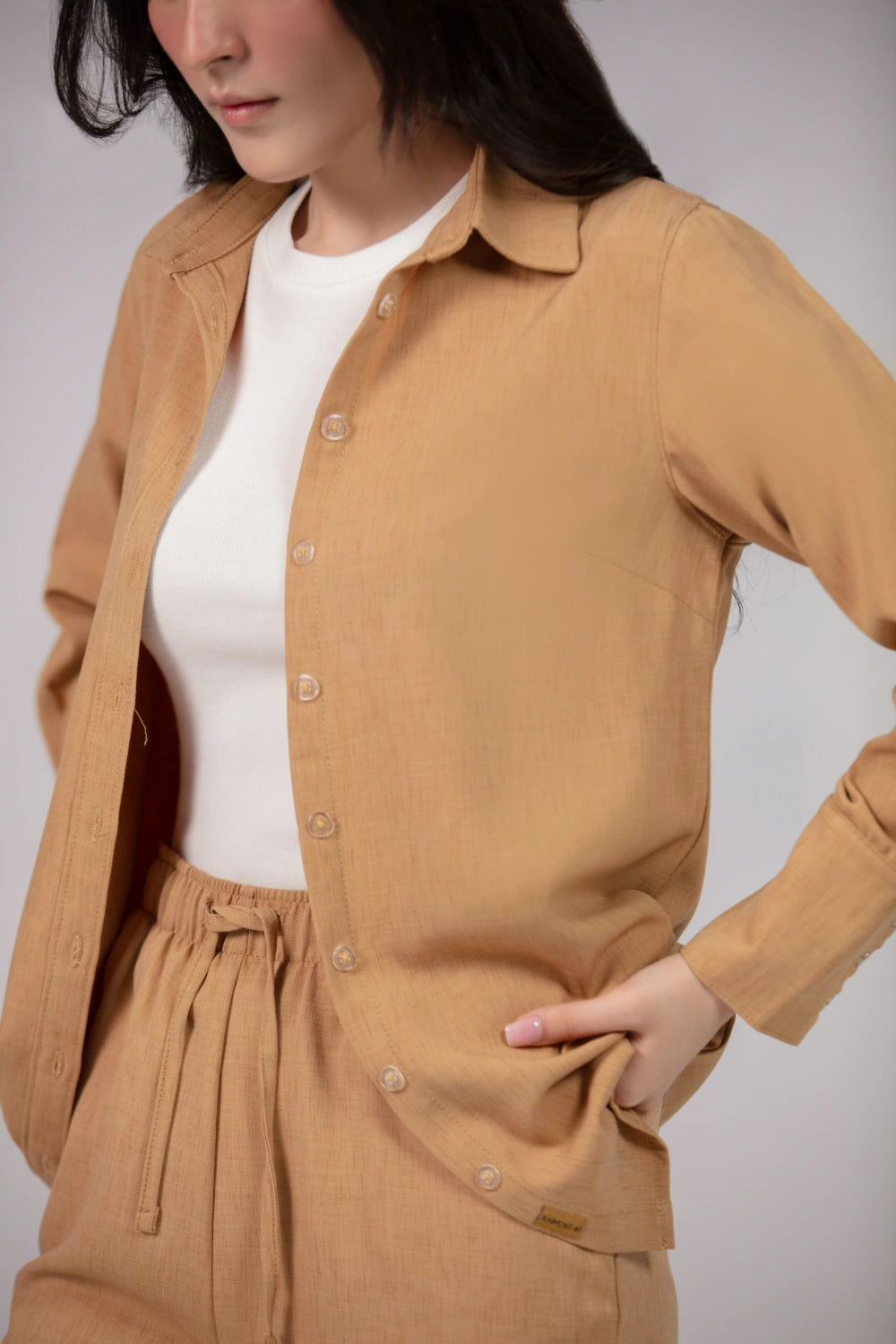 Person wearing a beige button-up shirt and pants on a plain background