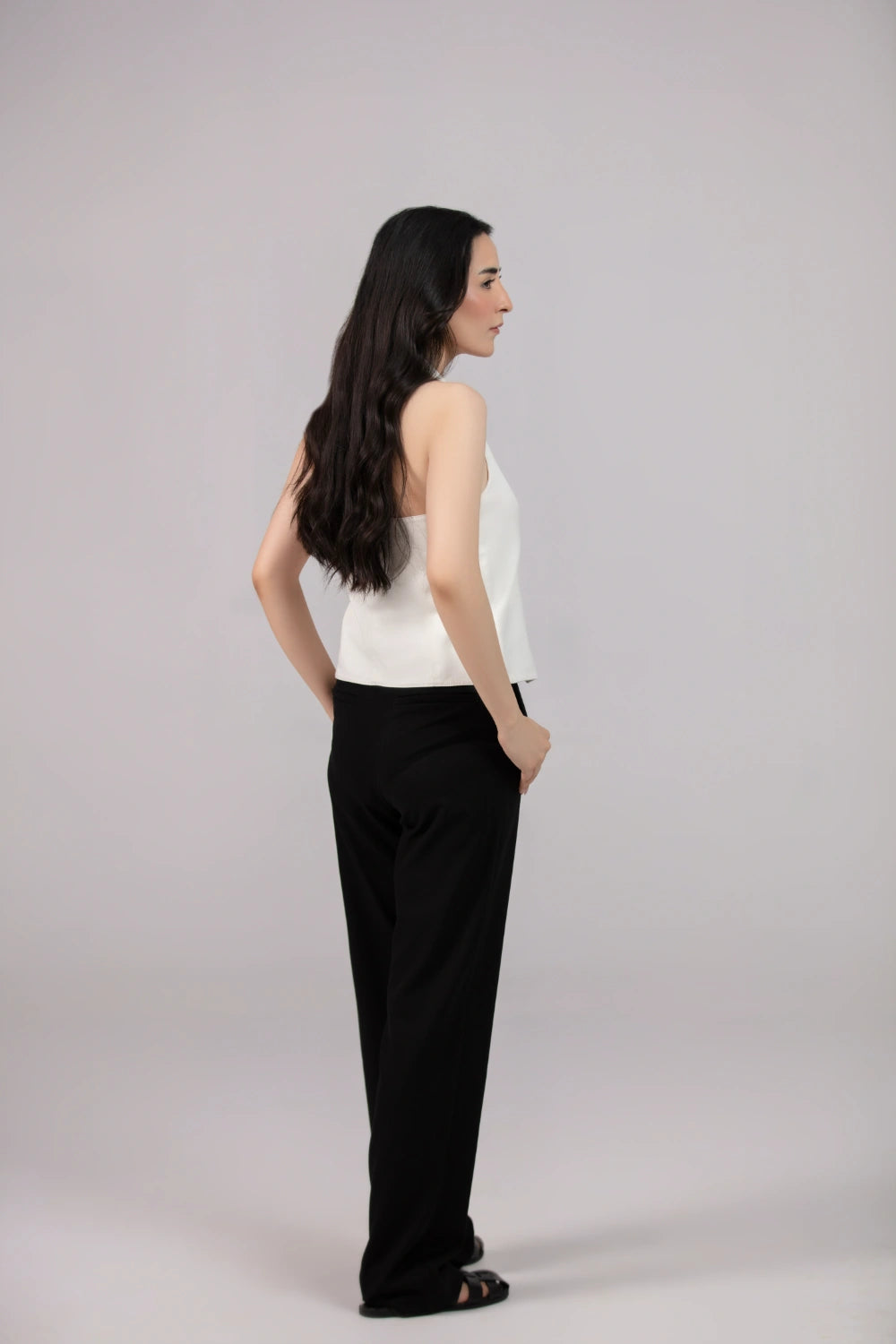 Woman wearing a white top and black pants on a gray background
