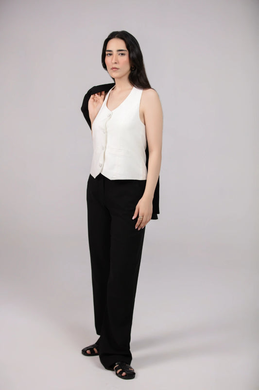Woman wearing a white vest over a black top with black pants on a plain background
