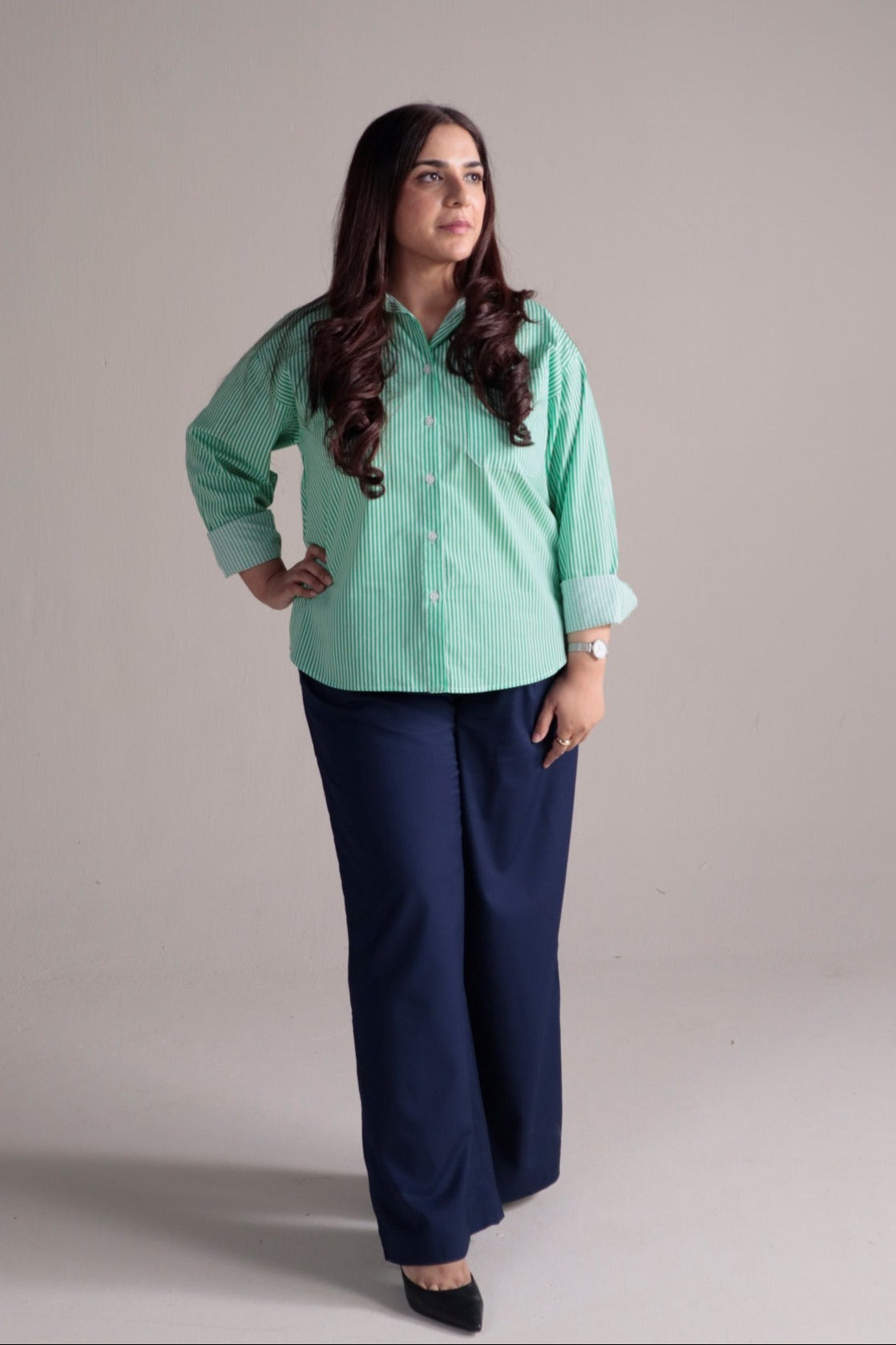 Person wearing a green shirt and navy wide leg pants on a plain background