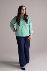 Person wearing a green shirt and navy wide leg pants on a plain background