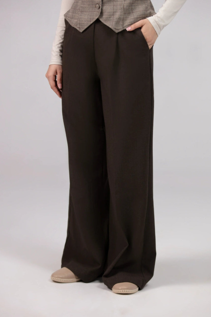 Person wearing a gray checkered vest and brown wide-leg pants on a white background